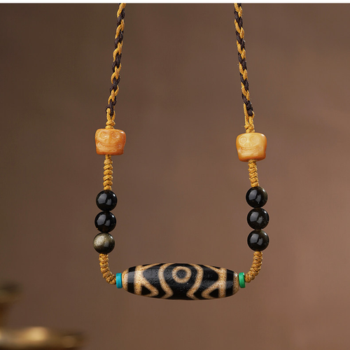 Front view of the Inner Compass cord necklace with a cream eye-pattern focal bead, black round accents and amber-colored sculpted faces.