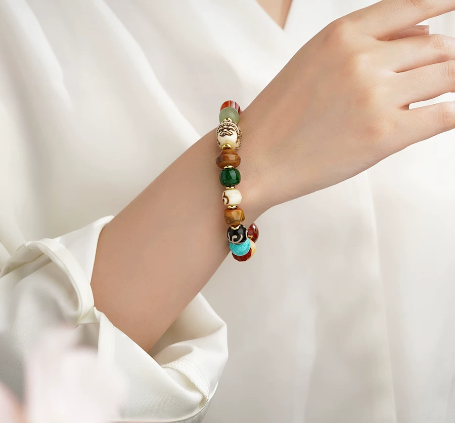 Many Wishes multicolor bracelet worn with a white sleeve, showing patterned beads, a sculpted face and gold-tone spacers.