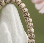 Close view of cream barrel-shaped beads with dark scattered speckles resting on a pale stone surface.