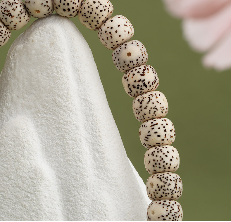 Close view of cream barrel-shaped beads with dark scattered speckles resting on a pale stone surface.