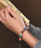 Multicolor bead bracelet on a wrist beside a folding fan, with glossy colored beads, sculpted details and gold-tone spacers.
