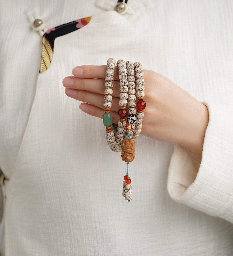 A hand holding the Star & Moon bead strand, showing cream speckled beads, red and green accents and teal cord ends.